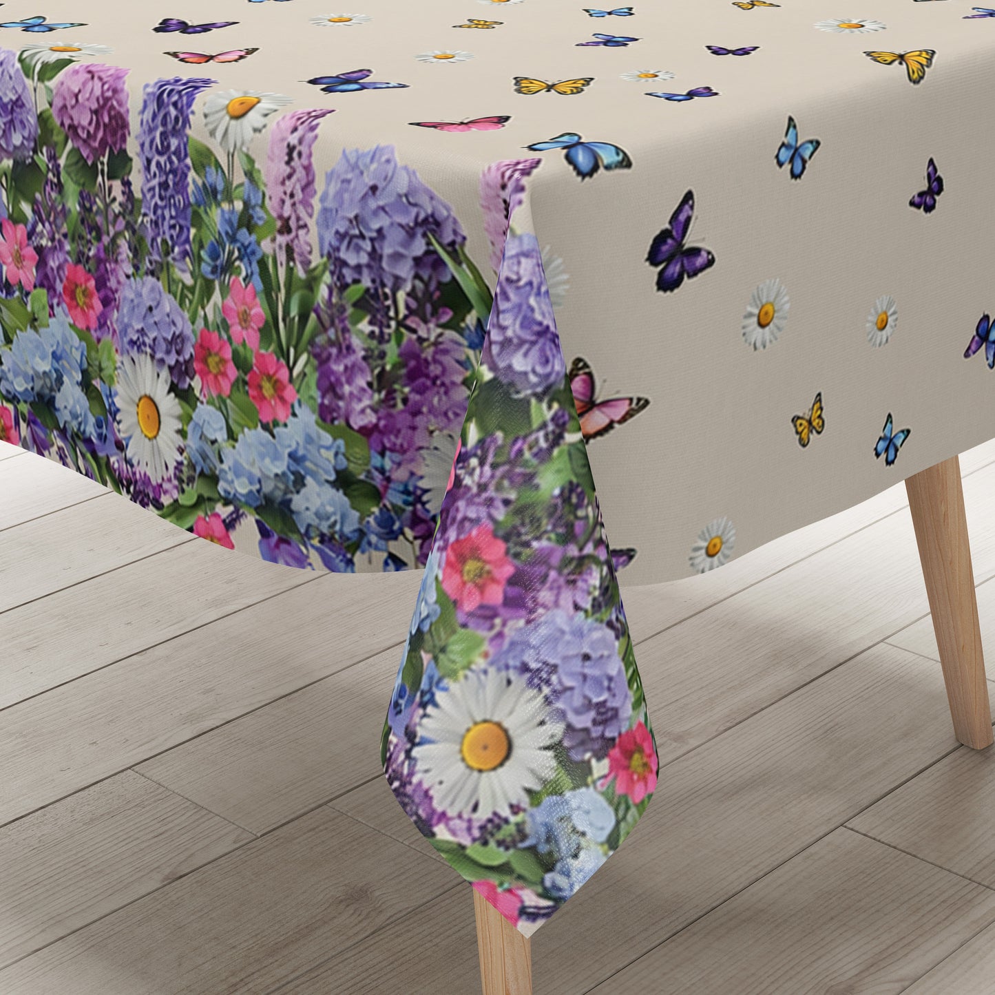 Wachstuch-Tischdecke mit cremefarbenem Hintergrund, dekoriert mit bunten Schmetterlingen und weißen Margeriten. Entlang der Ränder verläuft eine üppige Blumenbordüre aus Lavendel, Hortensien und weiteren Blüten in Violett-, Blau-, Rosa- und Weißtönen. Das frühlingshafte Design erinnert an eine blühende Gartenwiese und sorgt für eine freundliche, sommerliche Atmosphäre.