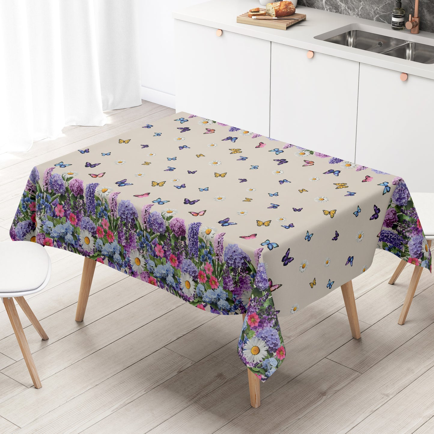 Wachstuch-Tischdecke mit cremefarbenem Hintergrund, dekoriert mit bunten Schmetterlingen und weißen Margeriten. Entlang der Ränder verläuft eine üppige Blumenbordüre aus Lavendel, Hortensien und weiteren Blüten in Violett-, Blau-, Rosa- und Weißtönen. Das frühlingshafte Design erinnert an eine blühende Gartenwiese und sorgt für eine freundliche, sommerliche Atmosphäre.