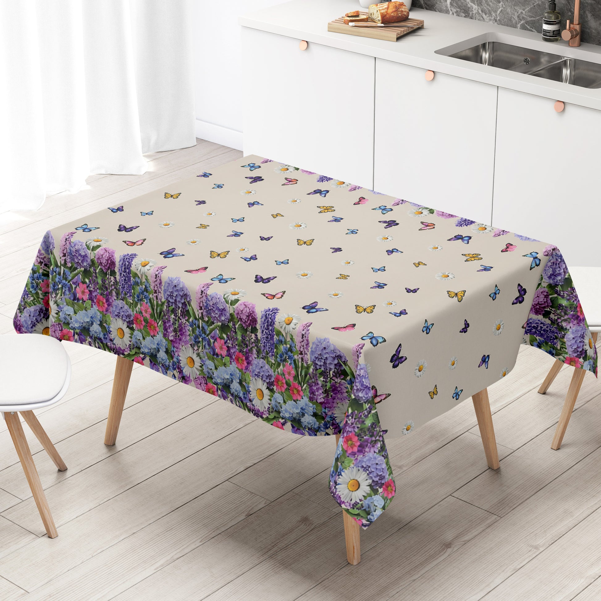 Wachstuch-Tischdecke mit cremefarbenem Hintergrund, dekoriert mit bunten Schmetterlingen und weißen Margeriten. Entlang der Ränder verläuft eine üppige Blumenbordüre aus Lavendel, Hortensien und weiteren Blüten in Violett-, Blau-, Rosa- und Weißtönen. Das frühlingshafte Design erinnert an eine blühende Gartenwiese und sorgt für eine freundliche, sommerliche Atmosphäre.