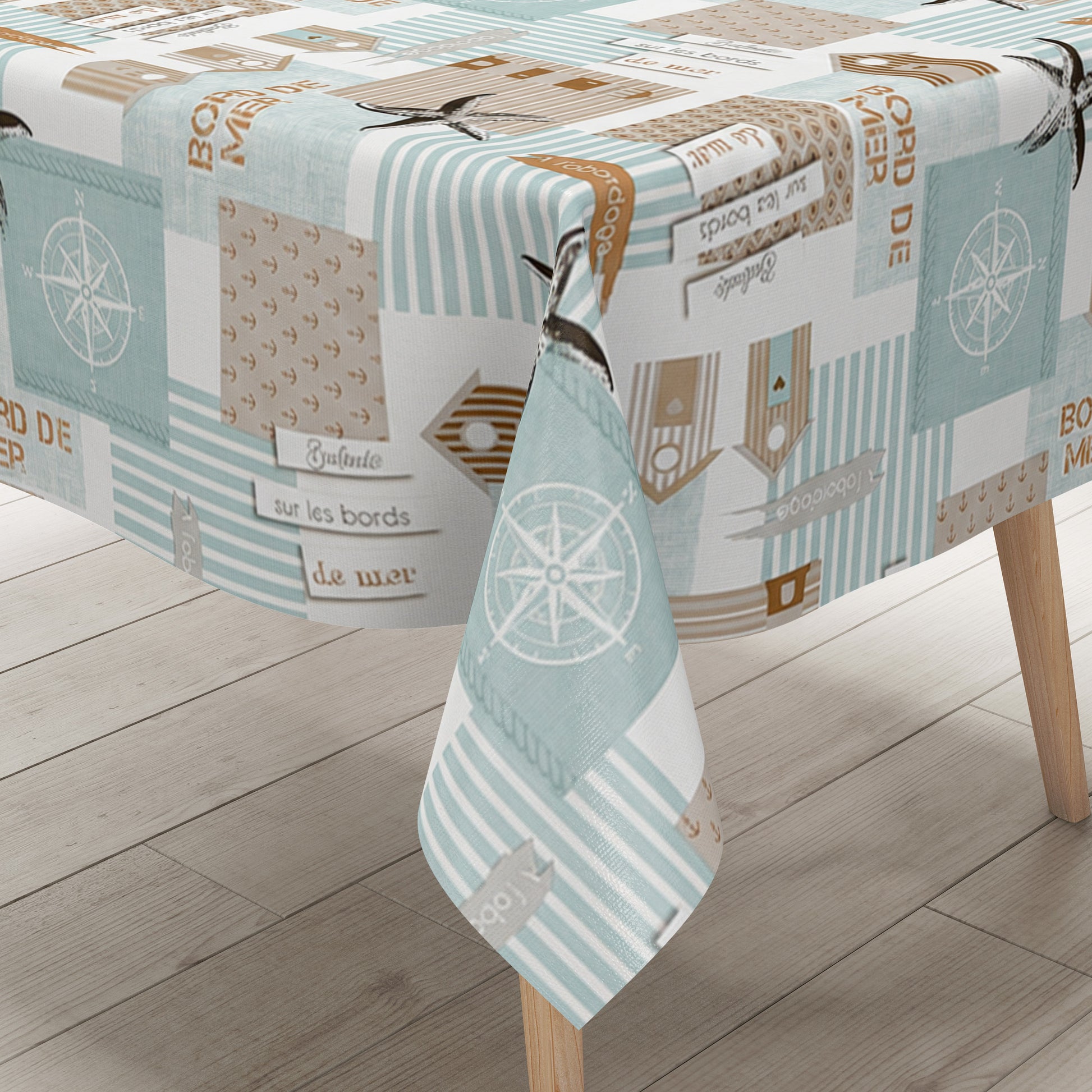 Maritime Wachstuch-Tischdecke mit Patchwork-Muster in Türkis, Beige und Weiß, verziert mit Strandhäusern, Seesternen, Kompassrosen, Streifen und dekorativen Schriftzügen im Küstenstil.
