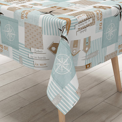 Maritime Wachstuch-Tischdecke mit Patchwork-Muster in Türkis, Beige und Weiß, verziert mit Strandhäusern, Seesternen, Kompassrosen, Streifen und dekorativen Schriftzügen im Küstenstil.