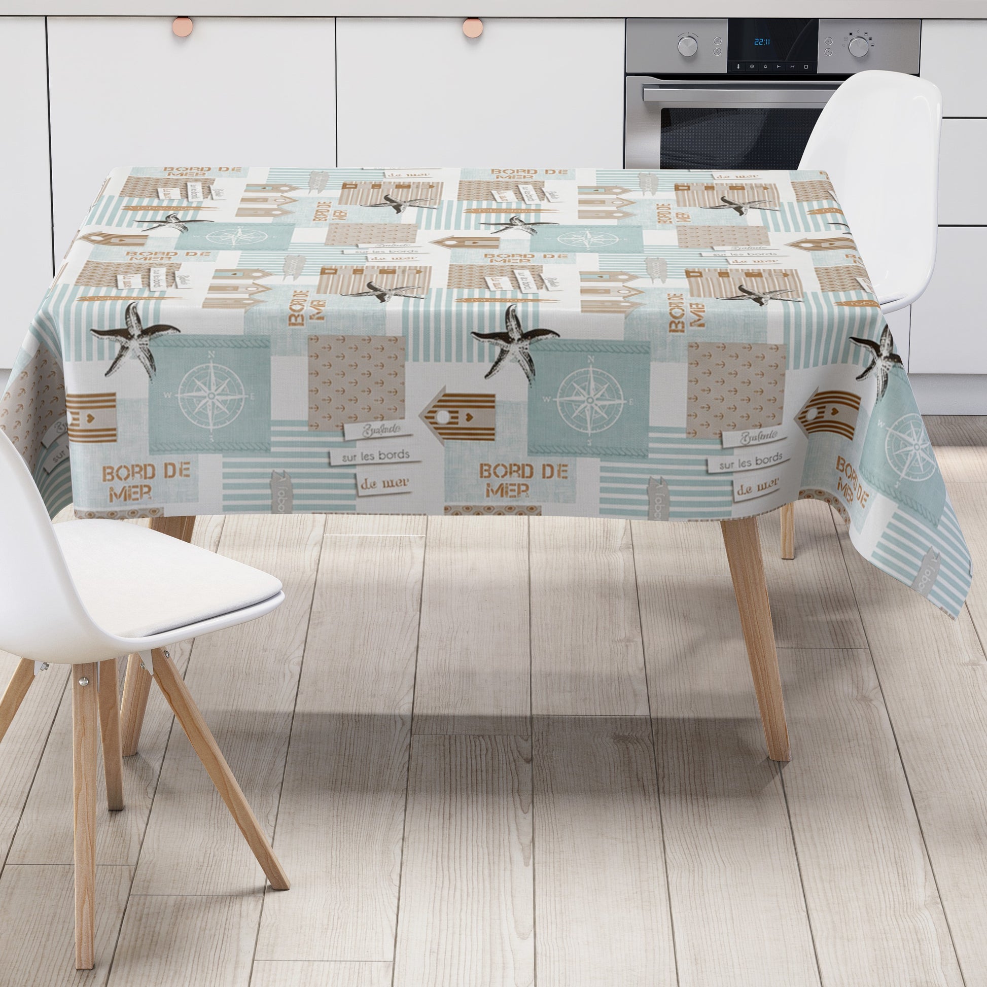 Maritime Wachstuch-Tischdecke mit Patchwork-Muster in Türkis, Beige und Weiß, verziert mit Strandhäusern, Seesternen, Kompassrosen, Streifen und dekorativen Schriftzügen im Küstenstil.