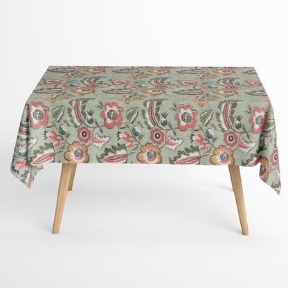 Beschichtete Baumwoll-Tischdecke mit floralem Muster auf olivgrünem Hintergrund, verziert mit großen Blüten in Korall-, Orange- und Cremetönen sowie dekorativen Blättern. Über eine Tischecke drapiert, mit sichtbaren hellen Holzbeinen.