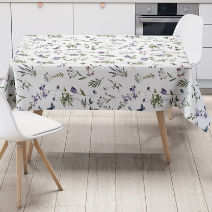 Weiße Wachstuch-Tischdecke mit zartem Wiesenblumen-Muster aus Wildblumen, Gräsern, Schmetterlingen und Libellen in sanften Violett-, Blau- und Grüntönen.