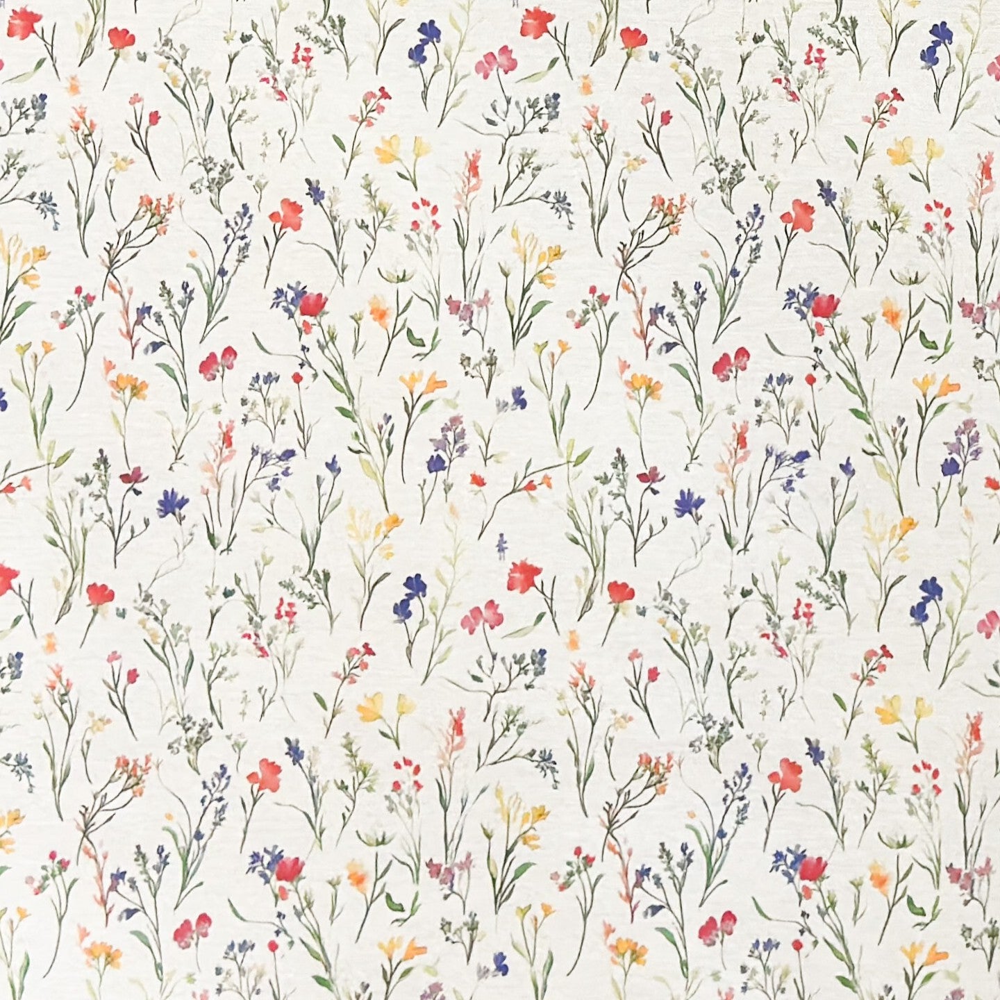 Beschichtete Baumwoll-Tischdecke mit zartem Streublumenmuster auf hellem Hintergrund. Filigrane Wildblumen und Gräser in Rot, Blau, Gelb und Rosa verteilen sich gleichmäßig über die Oberfläche. Über eine Tischecke drapiert, mit sichtbaren hellen Holzbeinen.