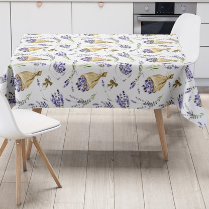 Wachstuch-Tischdecke mit Lavendelmuster auf hellem Hintergrund. Violette Lavendelzweige, kleine Sträuße und in Papier gewickelte Lavendelbouquets sind gleichmäßig verteilt und werden durch grüne Stiele sowie braune Details ergänzt.