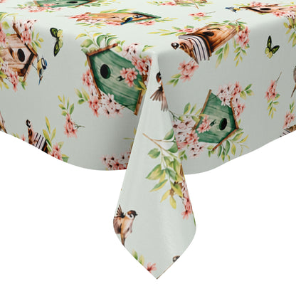 Wachstuch-Tischdecke mit Vogelhäuschen, kleinen Vögeln, Schmetterlingen und rosa Blüten auf hellem mintfarbenem Hintergrund. Grüne Blätter und natürliche Holztöne verleihen dem verspielten Frühlingsdesign eine frische, freundliche Ausstrahlung.