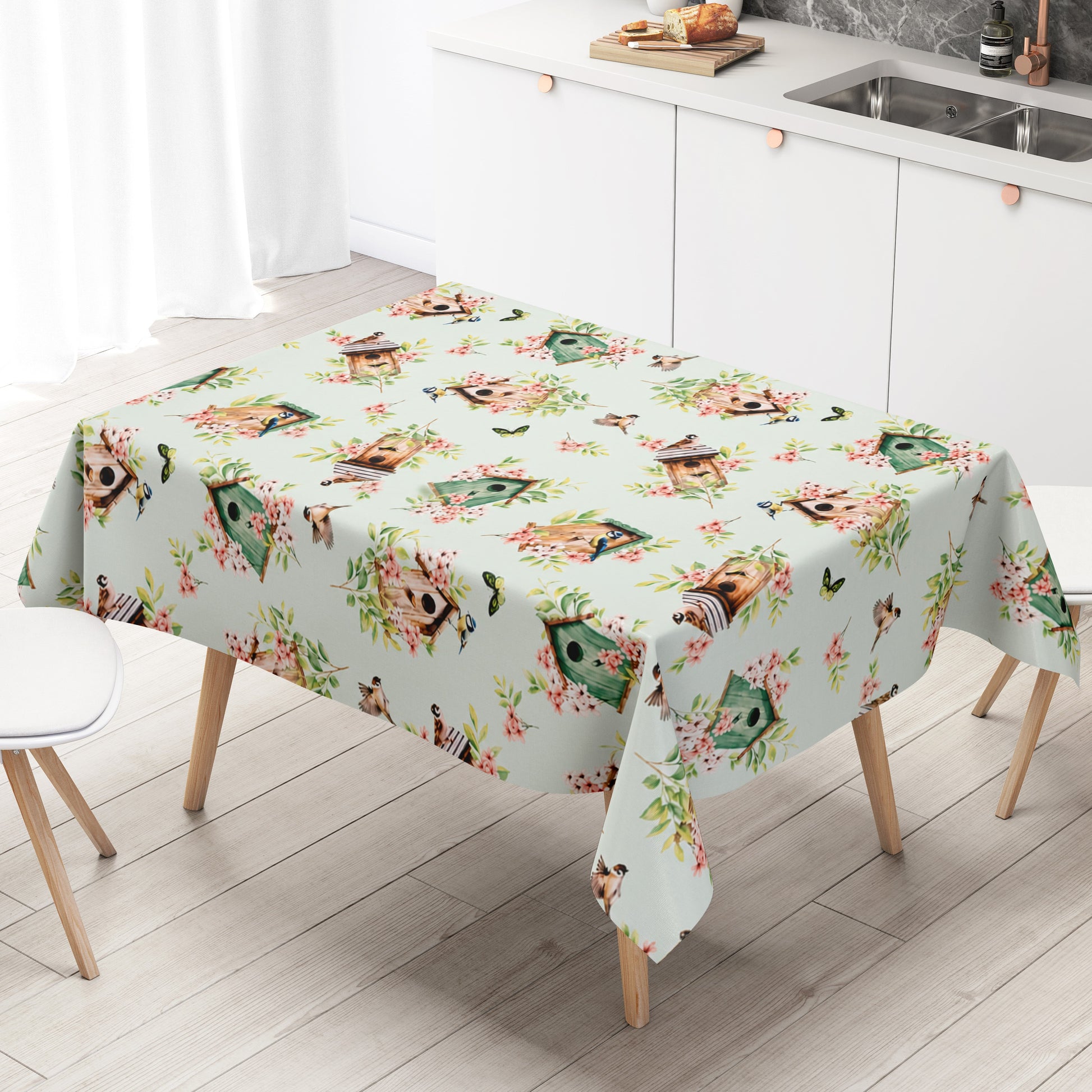 Wachstuch-Tischdecke mit Vogelhäuschen, kleinen Vögeln, Schmetterlingen und rosa Blüten auf hellem mintfarbenem Hintergrund. Grüne Blätter und natürliche Holztöne verleihen dem verspielten Frühlingsdesign eine frische, freundliche Ausstrahlung.