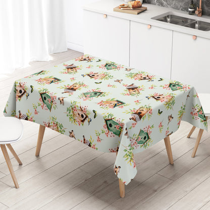 Wachstuch-Tischdecke mit Vogelhäuschen, kleinen Vögeln, Schmetterlingen und rosa Blüten auf hellem mintfarbenem Hintergrund. Grüne Blätter und natürliche Holztöne verleihen dem verspielten Frühlingsdesign eine frische, freundliche Ausstrahlung.