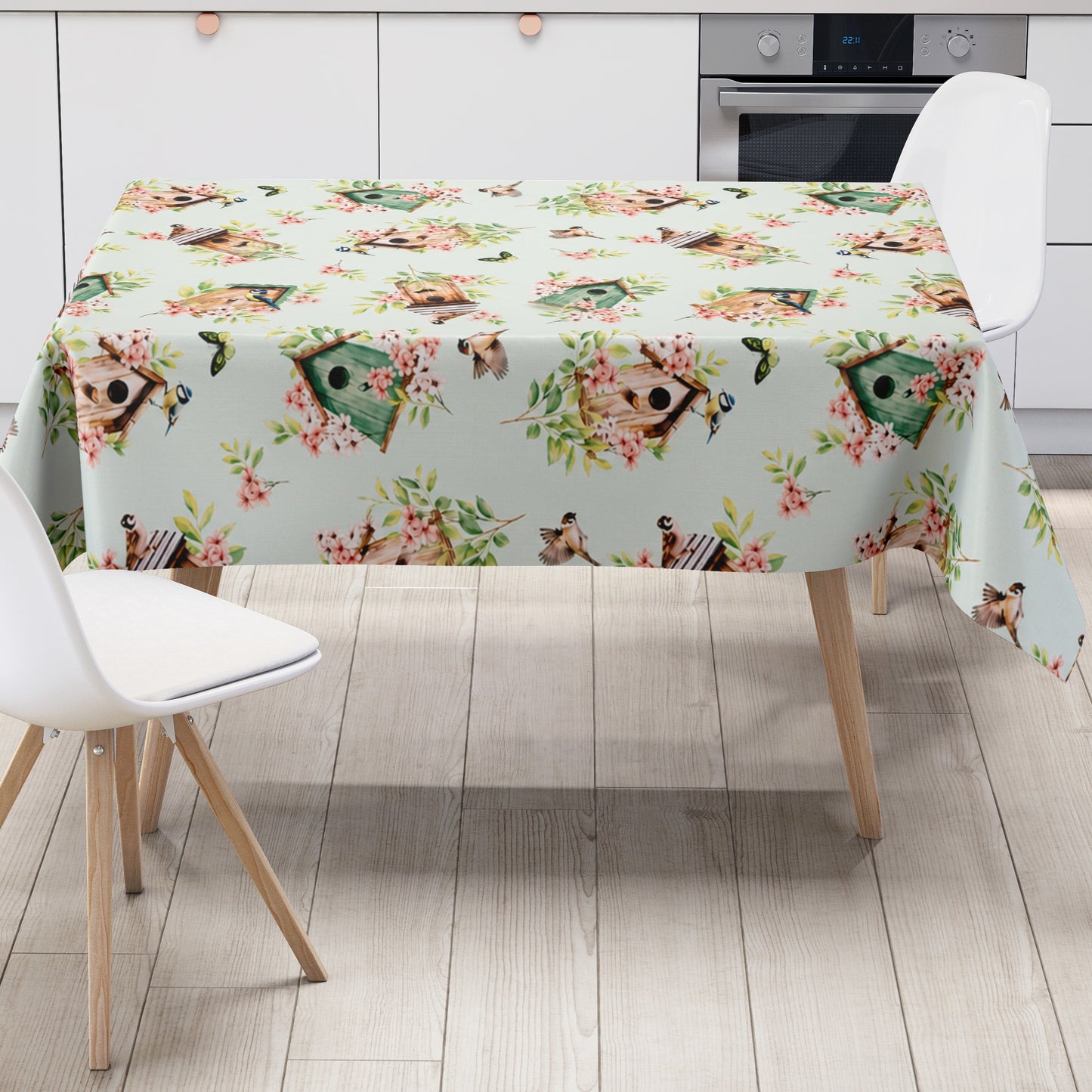 Wachstuch-Tischdecke mit Vogelhäuschen, kleinen Vögeln, Schmetterlingen und rosa Blüten auf hellem mintfarbenem Hintergrund. Grüne Blätter und natürliche Holztöne verleihen dem verspielten Frühlingsdesign eine frische, freundliche Ausstrahlung.