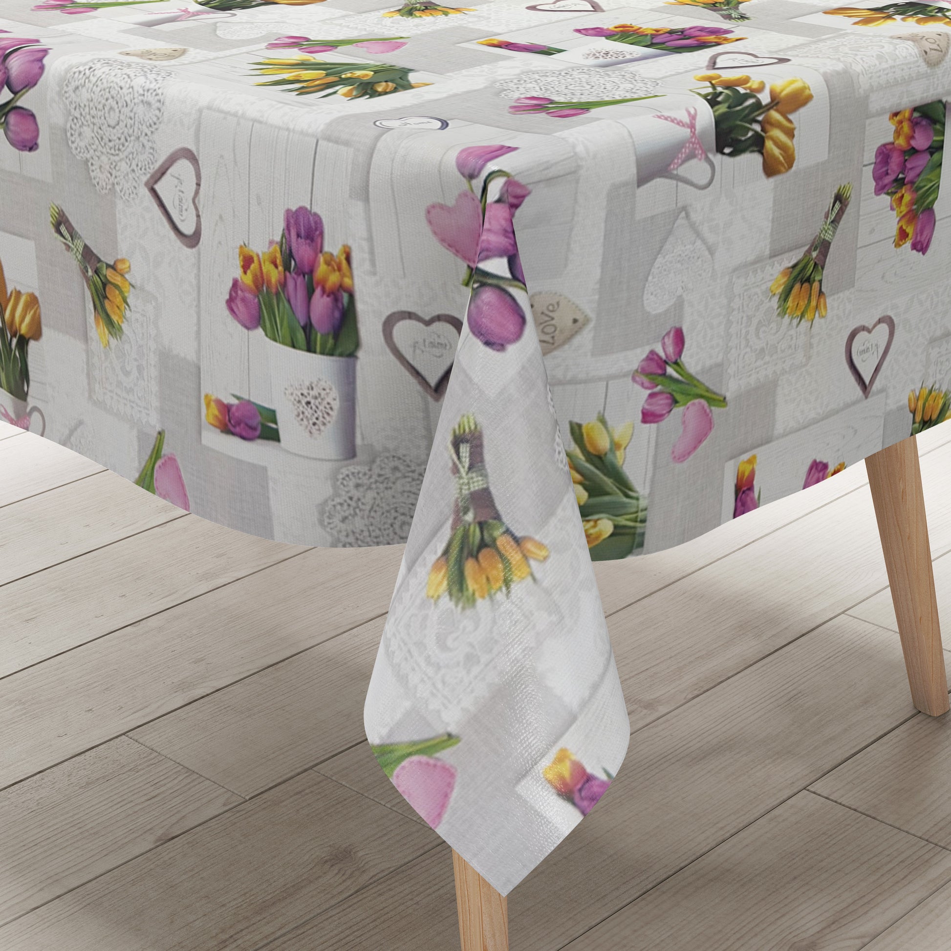 Wachstuch-Tischdecke mit romantischem Patchwork-Dessin in Hellgrau, Weiß und Creme. Das Muster zeigt rosa, violette und gelbe Tulpensträuße, Herzmotive, Spitzenornamente und Holzoptik-Elemente in harmonischer Anordnung. Die floralen Motive verleihen der Tischdecke einen frühlingshaften Landhausstil und schaffen eine freundliche, gemütliche Atmosphäre.