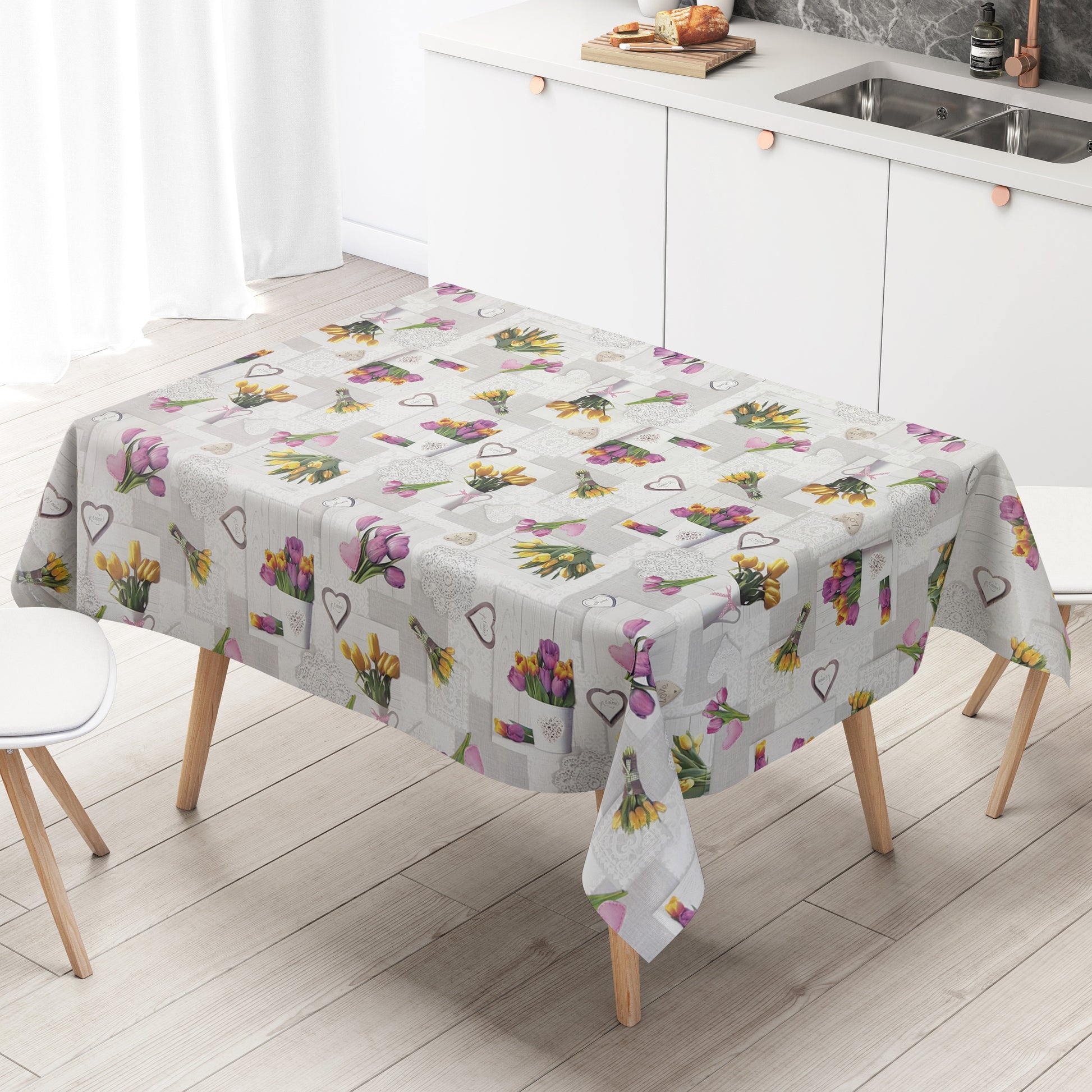 Wachstuch-Tischdecke mit romantischem Patchwork-Dessin in Hellgrau, Weiß und Creme. Das Muster zeigt rosa, violette und gelbe Tulpensträuße, Herzmotive, Spitzenornamente und Holzoptik-Elemente in harmonischer Anordnung. Die floralen Motive verleihen der Tischdecke einen frühlingshaften Landhausstil und schaffen eine freundliche, gemütliche Atmosphäre.