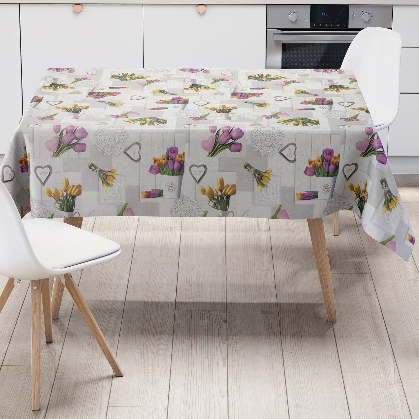 Wachstuch-Tischdecke mit romantischem Patchwork-Dessin in Hellgrau, Weiß und Creme. Das Muster zeigt rosa, violette und gelbe Tulpensträuße, Herzmotive, Spitzenornamente und Holzoptik-Elemente in harmonischer Anordnung. Die floralen Motive verleihen der Tischdecke einen frühlingshaften Landhausstil und schaffen eine freundliche, gemütliche Atmosphäre.