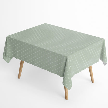 Salbeigrüne Tischdecke aus beschichteter Baumwolle mit Fleckenschutz und kleinen weißen Blattmustern, dekorativ über einem Tisch drapiert.
