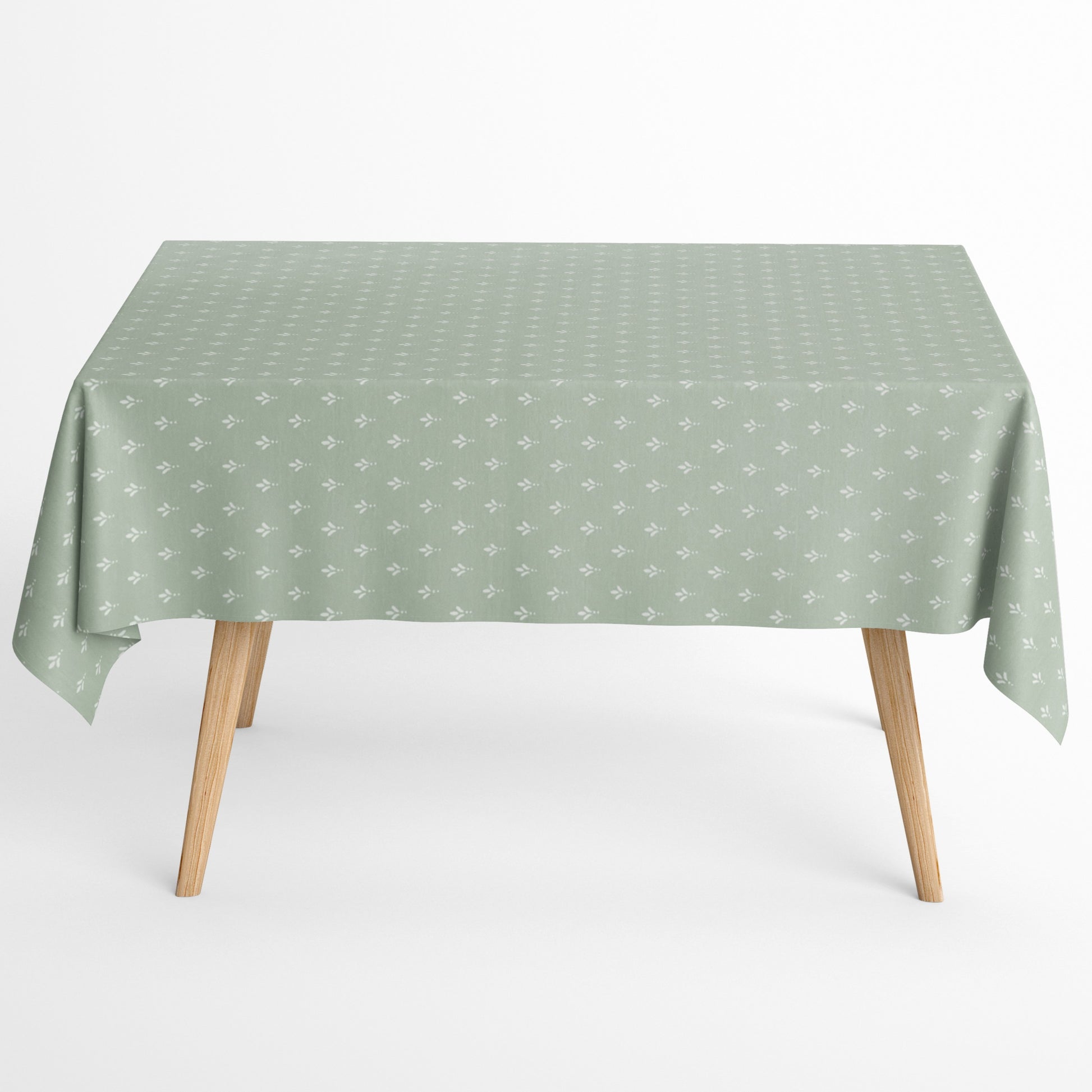 Salbeigrüne Tischdecke aus beschichteter Baumwolle mit Fleckenschutz und kleinen weißen Blattmustern, dekorativ über einem Tisch drapiert.