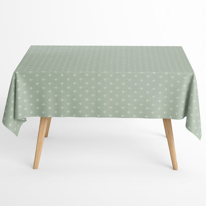 Salbeigrüne Tischdecke aus beschichteter Baumwolle mit Fleckenschutz und kleinen weißen Blattmustern, dekorativ über einem Tisch drapiert.