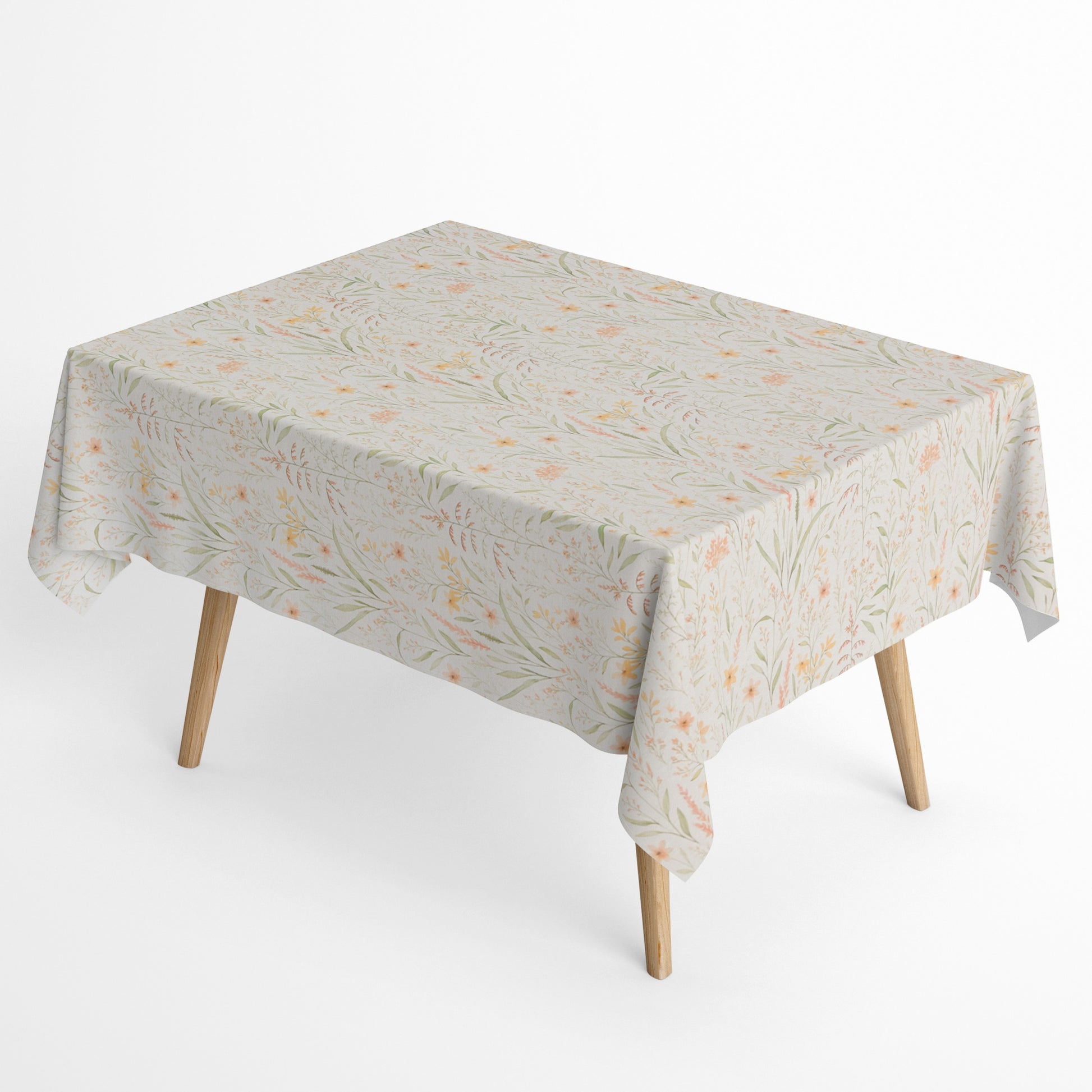 Beschichtete Baumwoll-Tischdecke mit filigranem Naturmuster auf hellem Hintergrund. Zarte Gräser, Blätter und kleine Blüten in Apricot-, Gelb- und Grüntönen verteilen sich gleichmäßig über die Oberfläche. Über eine Tischecke drapiert, mit sichtbaren hellen Holzbeinen.