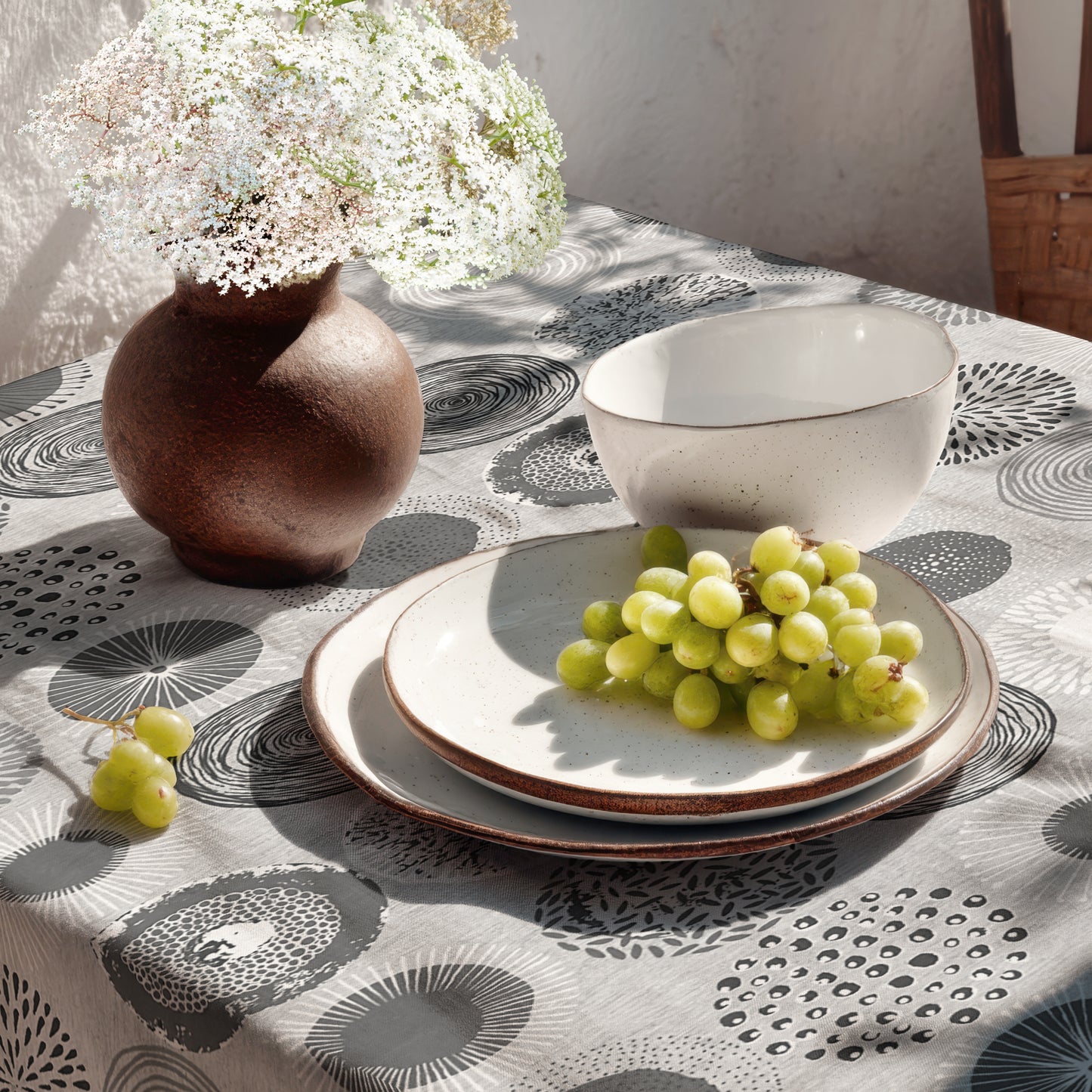 Jacquard-Tischdecke mit grafischem Kreismotiv aus Spiralen, Punkten, Strahlen und floralen Formen in Grau, Weiß und Anthrazit.