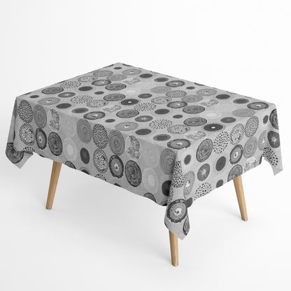 Jacquard-Tischdecke mit grafischem Kreismotiv aus Spiralen, Punkten, Strahlen und floralen Formen in Grau, Weiß und Anthrazit.