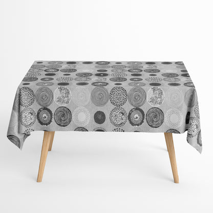 Jacquard-Tischdecke mit grafischem Kreismotiv aus Spiralen, Punkten, Strahlen und floralen Formen in Grau, Weiß und Anthrazit.