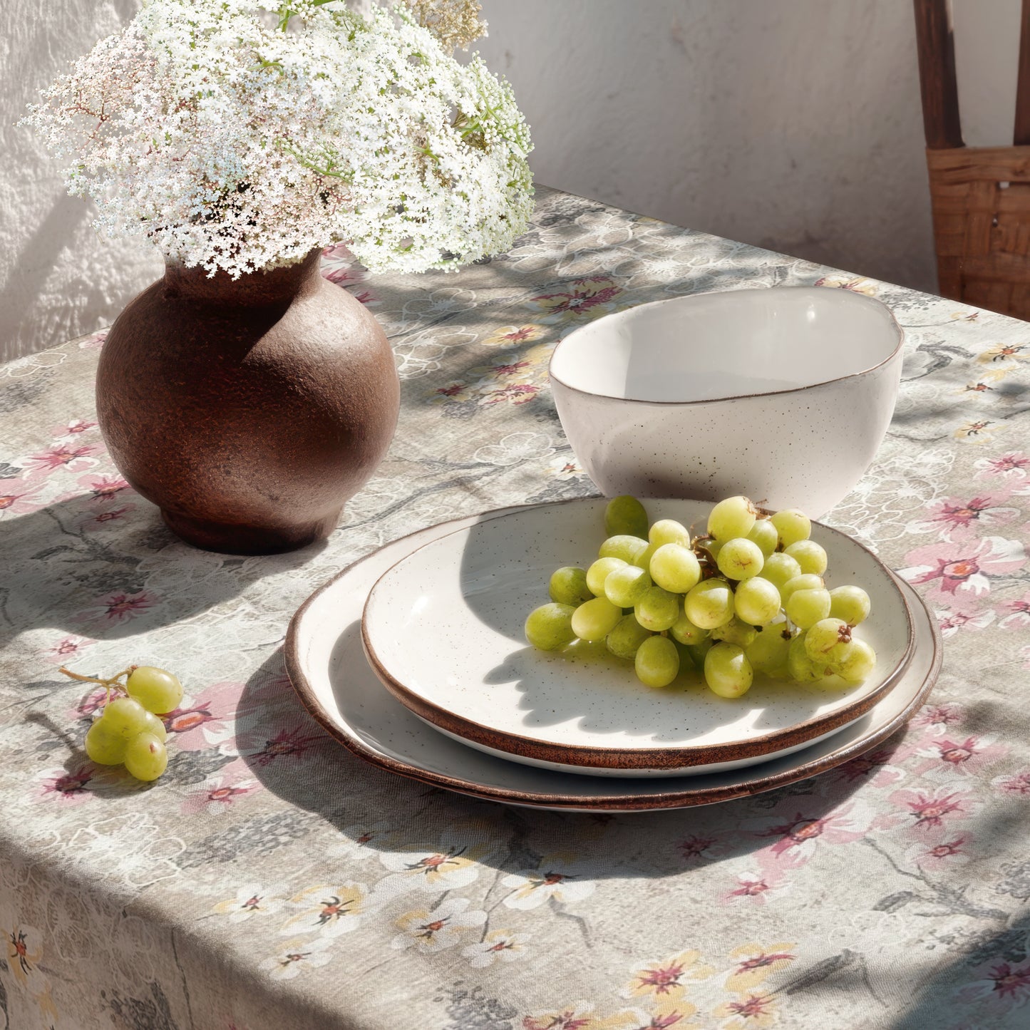 Beschichtete Baumwoll-Tischdecke mit Fleckenschutz im Design ROVIERA, naturfarbener Hintergrund mit zarten Kirschblüten in Weiß, Rosa und Creme auf filigranen Zweigen sowie dekorativen floralen Konturen in Beige- und Grautönen.