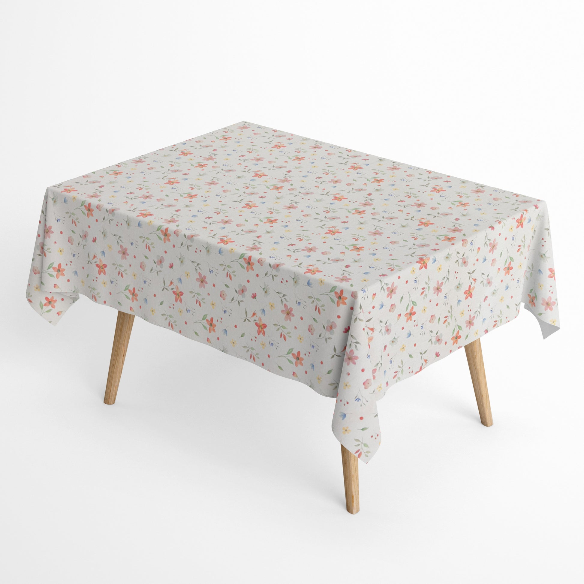 Beschichtete Baumwoll-Tischdecke mit zartem Streublumenmuster auf hellem Hintergrund. Kleine Blüten, feine Zweige und dekorative Punkte in Rosa, Korall, Gelb, Blau und Grün verteilen sich gleichmäßig über die Oberfläche. Über eine Tischecke drapiert, mit sichtbaren hellen Holzbeinen.
