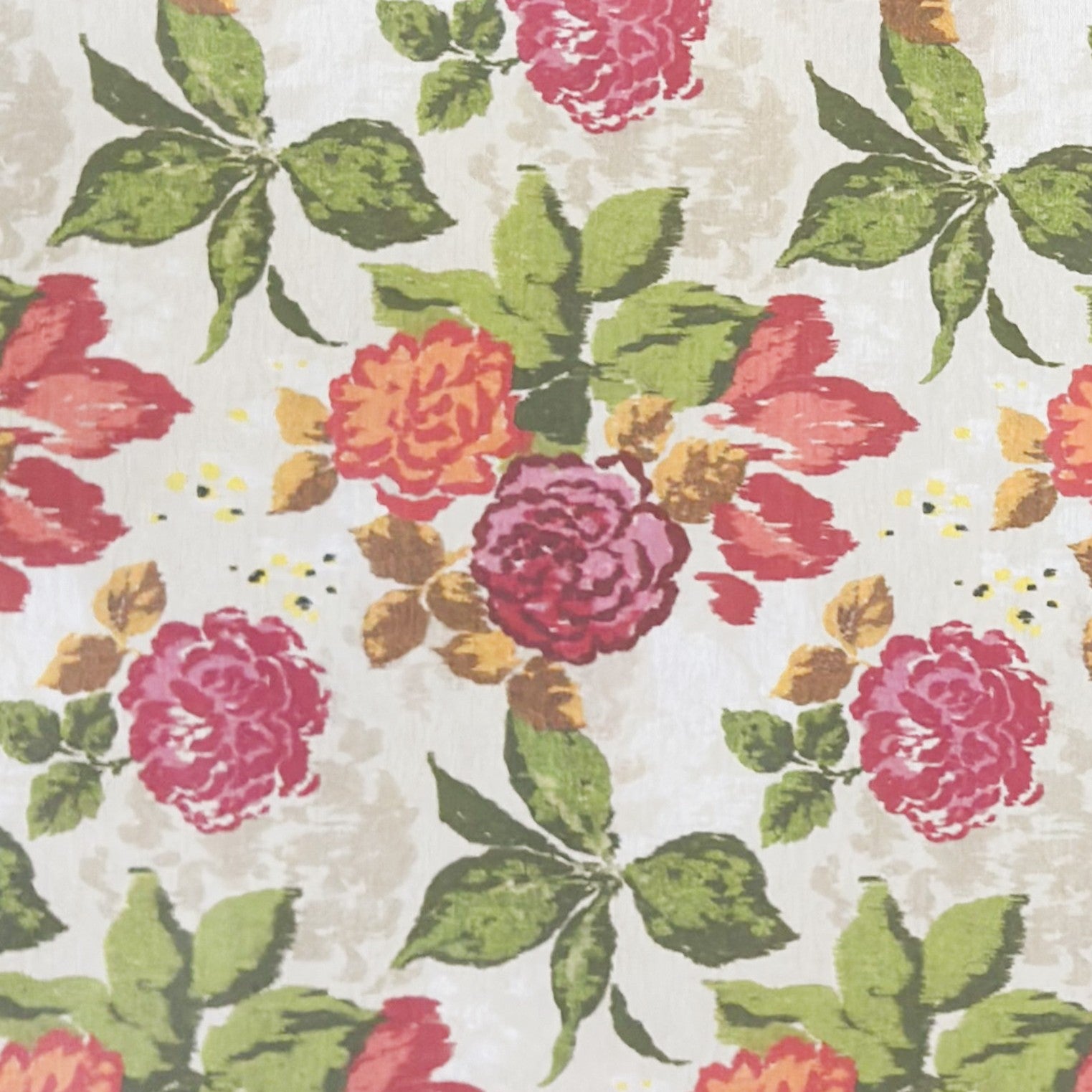 Beschichtete Baumwoll-Tischdecke mit großem floralem Muster auf hellem Hintergrund. Auffällige Blüten in Pink, Rot und Orange sowie grüne Blätter verteilen sich über die Oberfläche. Über eine Tischecke drapiert, mit sichtbaren hellen Holzbeinen.